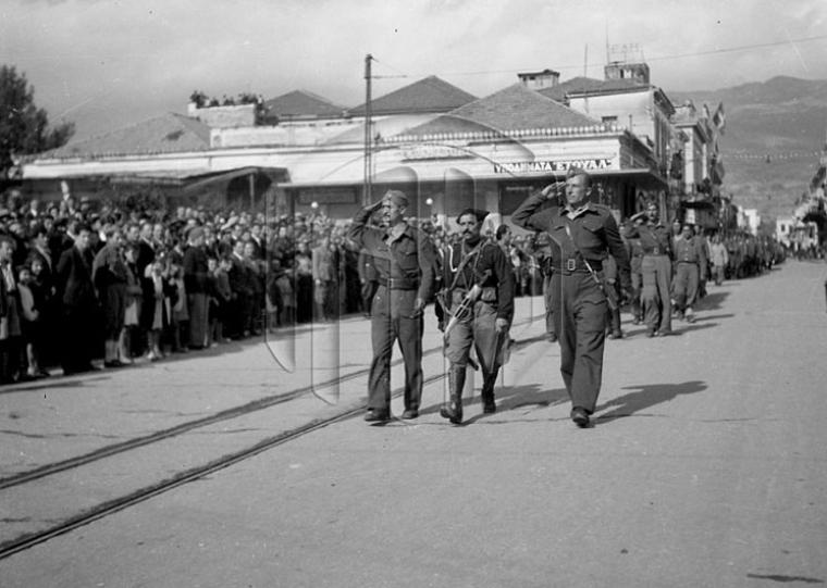 Φωτό Αρχεία Νομού Μεσσηνίας - Γενικά Αρχεία του Κράτους.  1944 10 28 11. Παρέλαση στην οδό Αριστομένους. Στη φωτογραφία εν μέσω δύο ανταρτών παρελαύνει ο διοικητής του ΙΙ Τάγματος του 8ου Συντάγματος, λοχαγός Γεώργιος Αρετάκης, γνωστός με το ψευδώνυμο «Σφακιανός», λόγω της κρητικής του καταγωγής (28-10-1944)